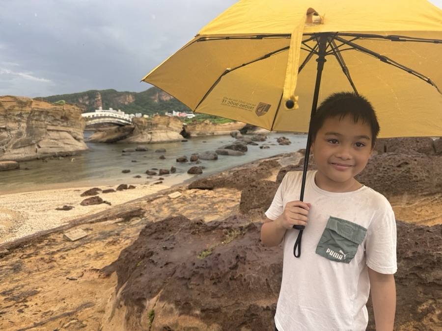 Liam smiling under a yellow umbrella by the sea